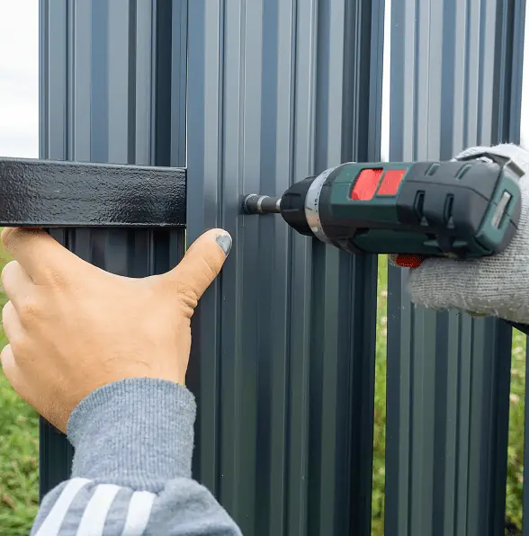 man using screwdriver twists metal picket fence