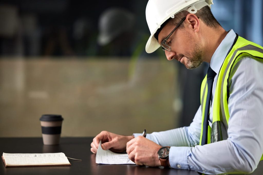 Restoration contractor in hard hat and safety vest reviewing insurance supplement paperwork at office desk